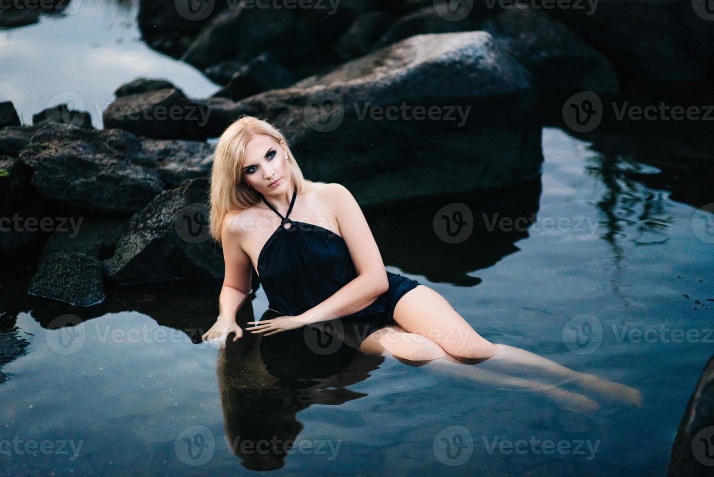 blonde girl in a black dress with blue eyes on the coast of the river photo