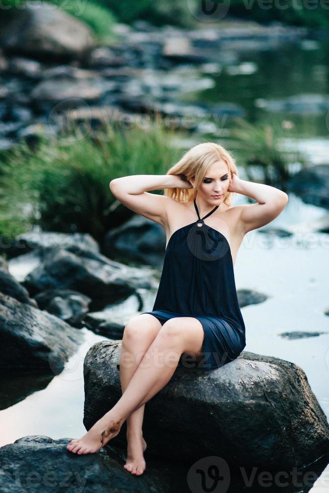 blonde girl in a black dress with blue eyes on the coast of the river photo