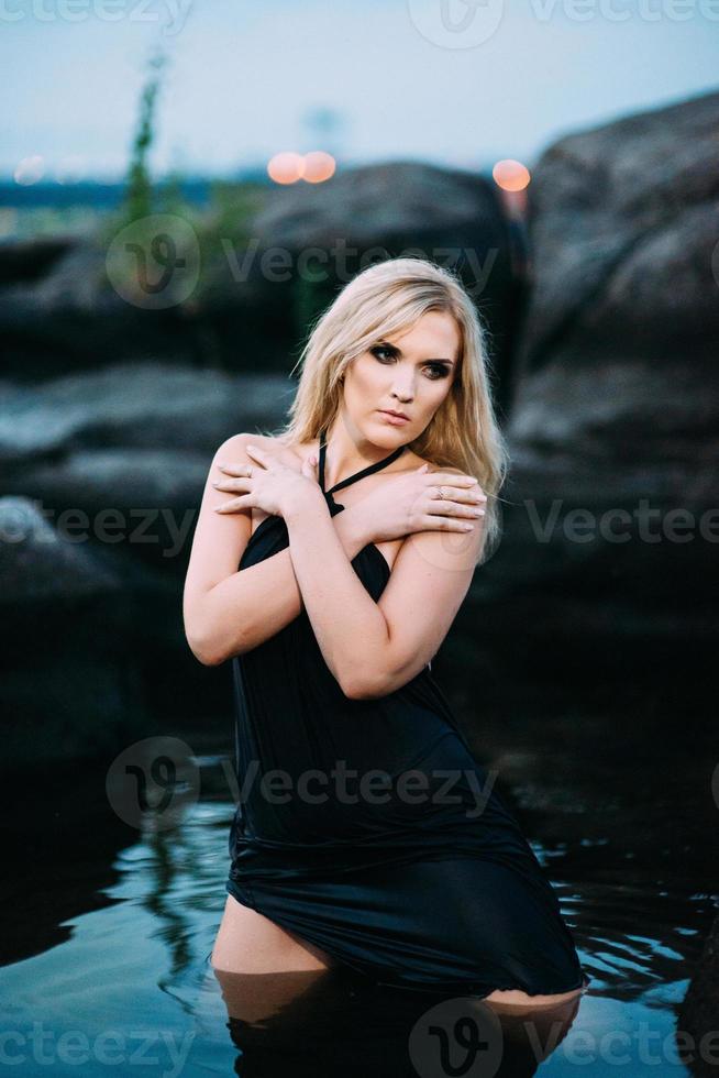 chica rubia con un vestido negro con ojos azules en la costa del río foto