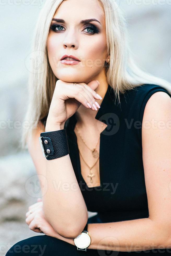 blonde girl in a black trouser suit with blue eyes on the background of a granite quarry photo