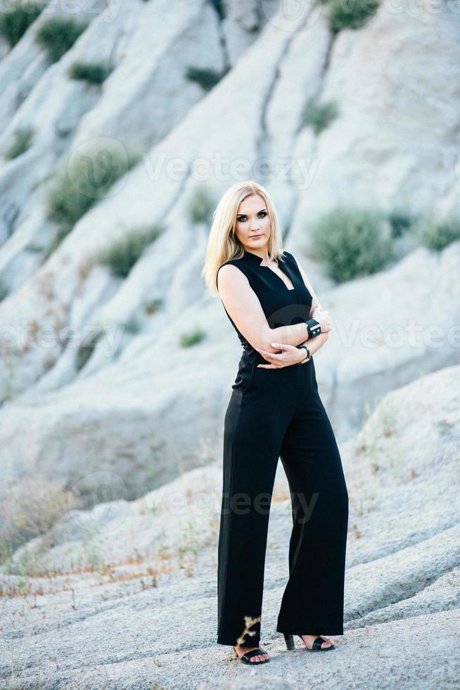 blonde girl in a black trouser suit with blue eyes on the background of a granite quarry photo