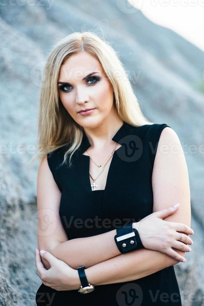 Chica rubia en un traje pantalón negro con ojos azules en el fondo de una cantera de granito foto