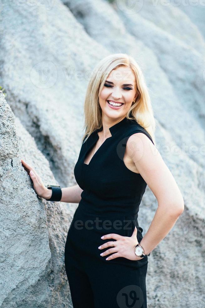 blonde girl in a black trouser suit with blue eyes on the background of a granite quarry photo