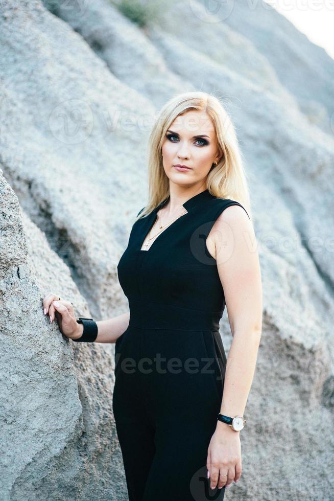 blonde girl in a black trouser suit with blue eyes on the background of a granite quarry photo