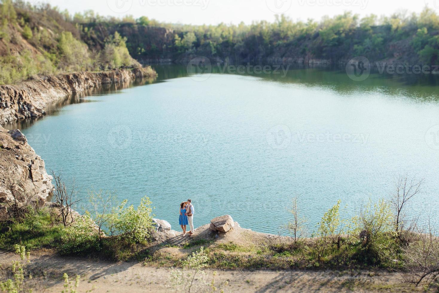 una pareja joven, un chico y una chica caminan cerca de un lago de montaña rodeado foto