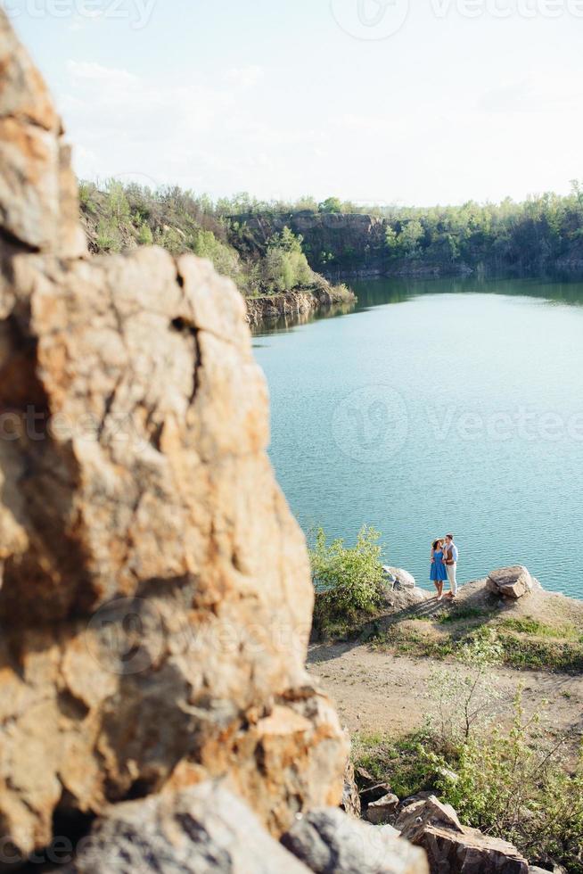 una pareja joven, un chico y una chica caminan cerca de un lago de montaña rodeado foto