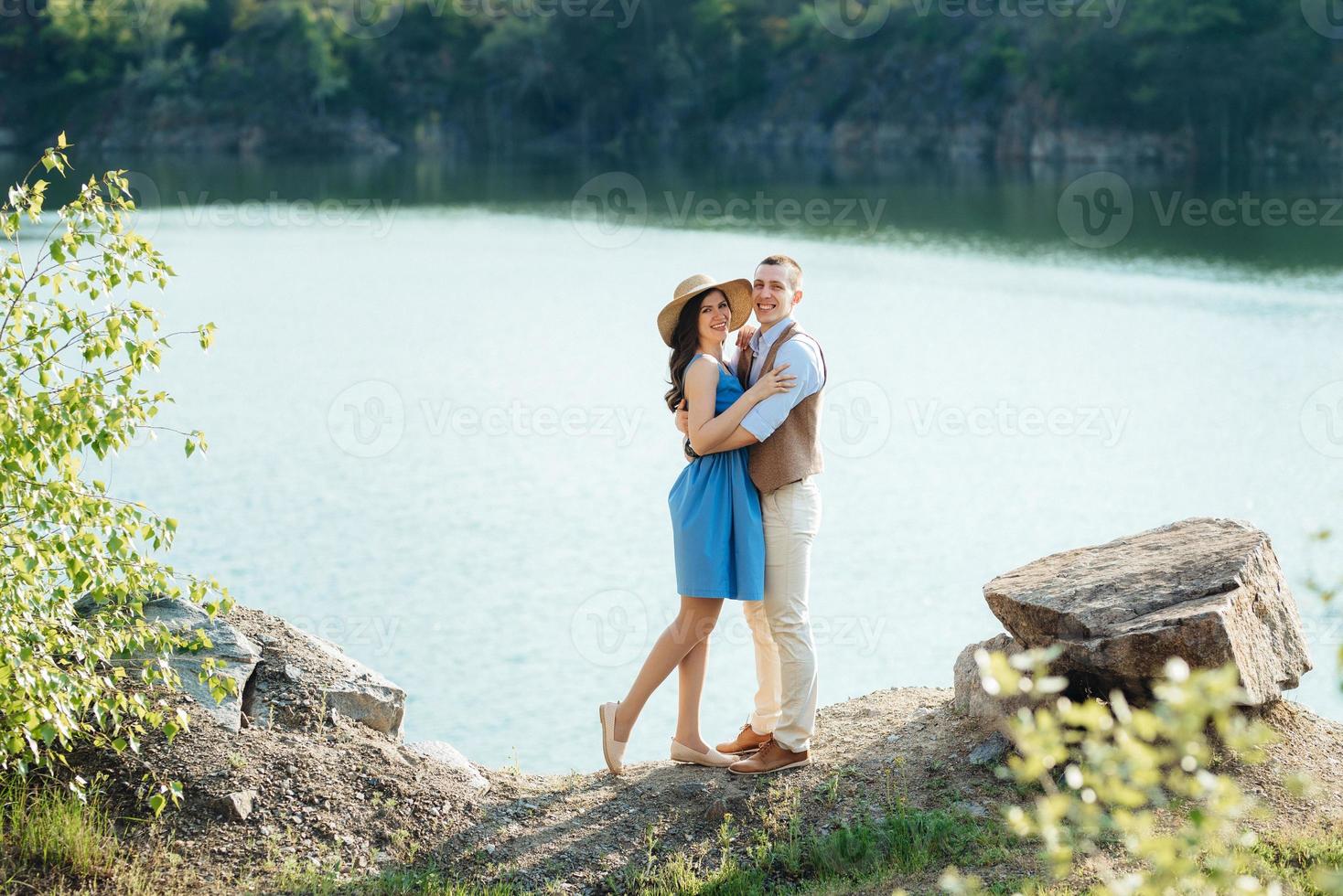 una pareja joven, un chico y una chica caminan cerca de un lago de montaña rodeado foto