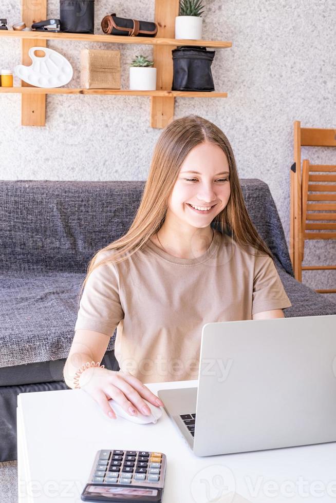 Adolescente femenina sonriente estudiando usando su computadora portátil en casa foto