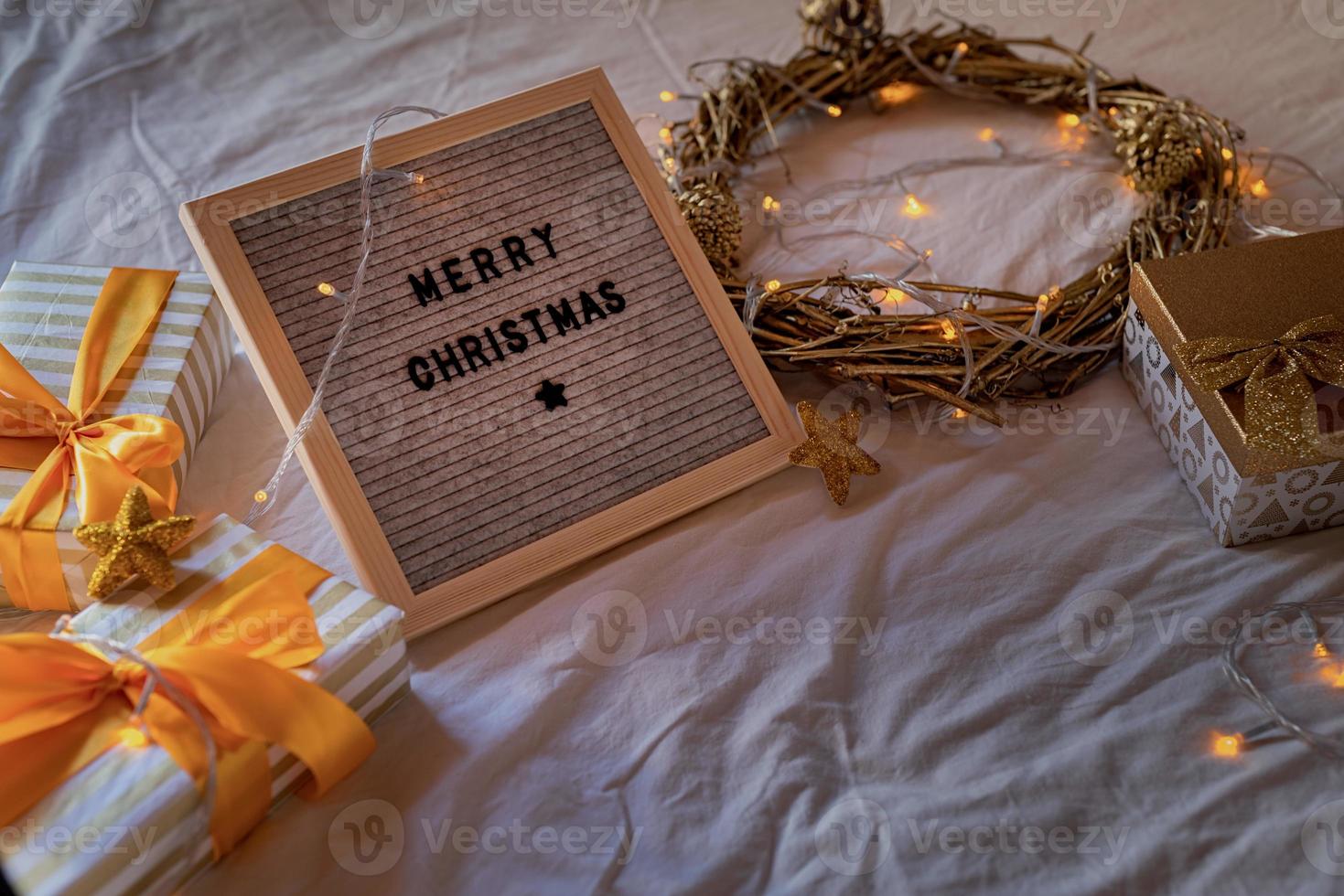 Felt letter board on the bed decorated with golden wreath, lights and gift boxes photo