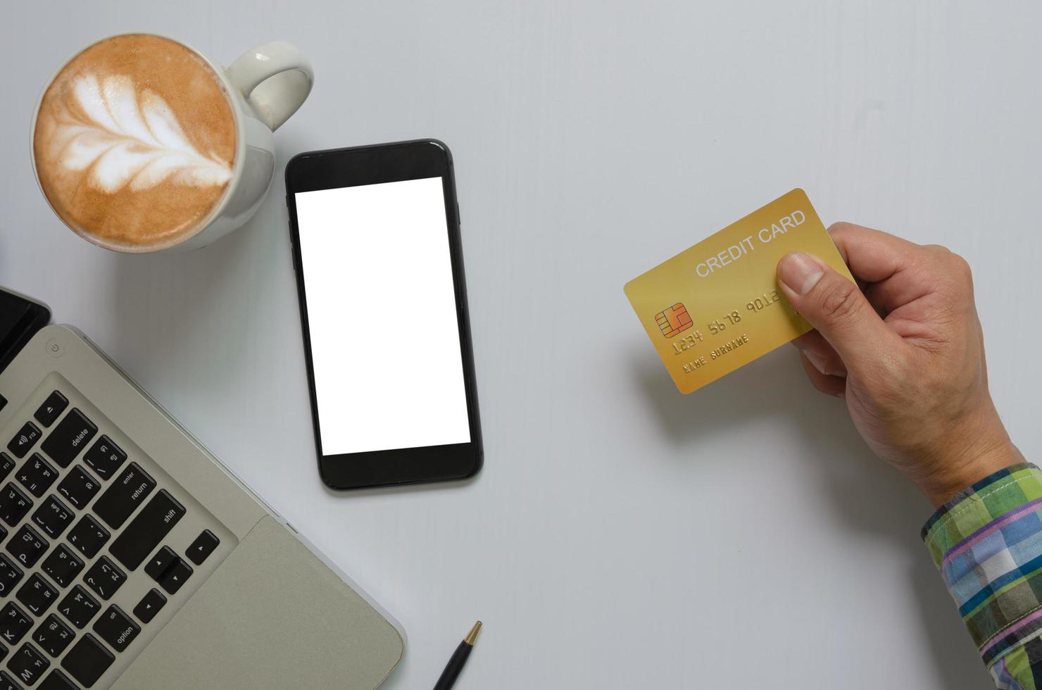 Vista superior de un hombre que sostiene un teléfono móvil con tarjeta de crédito simulacro de pantalla en blanco en blanco y tecnología de comunicación empresarial de computadora y café, concepto de compras en línea. foto