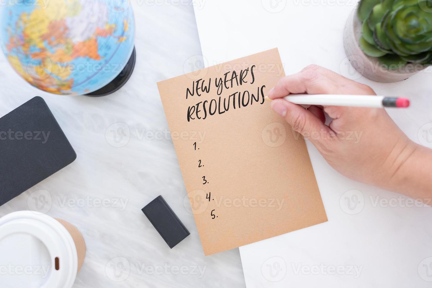 Hand holding pen writing on brown paper with blue globe,blackboard,coffee cup on marble table photo