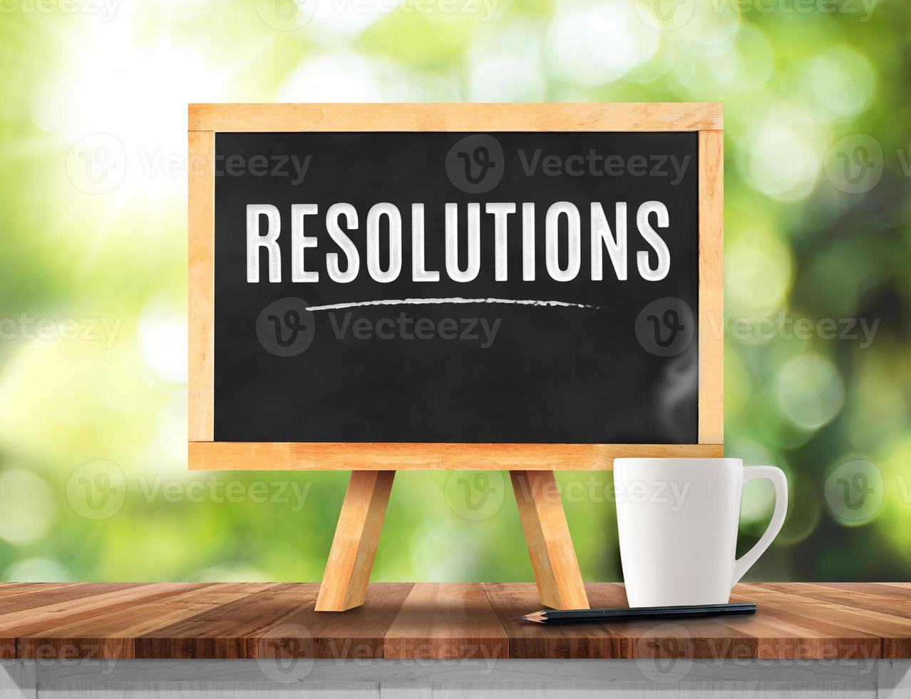 Resolutions word on Blackboard with easel on brown wood table top with sun and blur photo