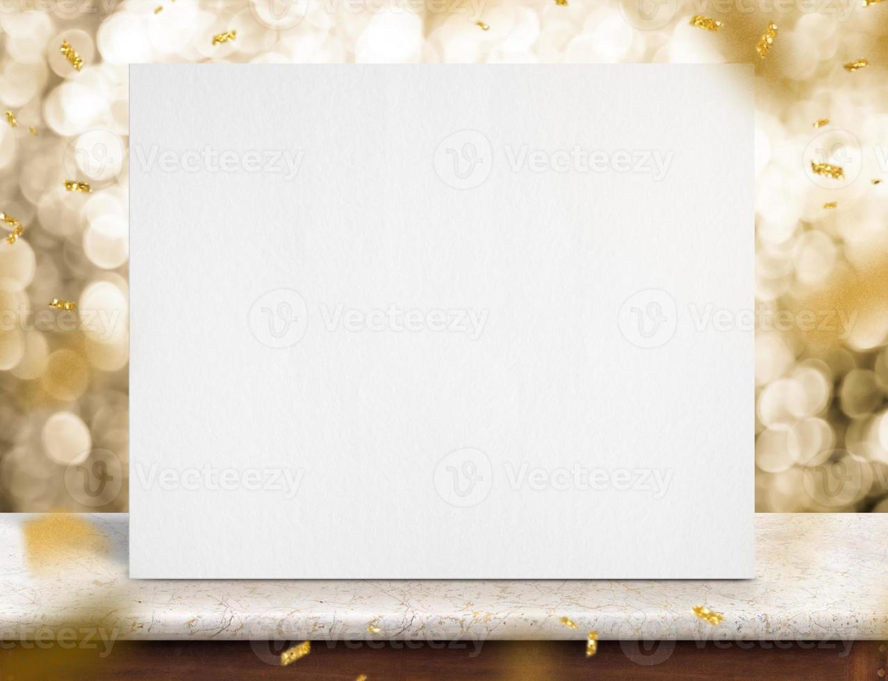Blank white paper poster on marble table with gold sparkling confetti at gold bokeh lights at background photo