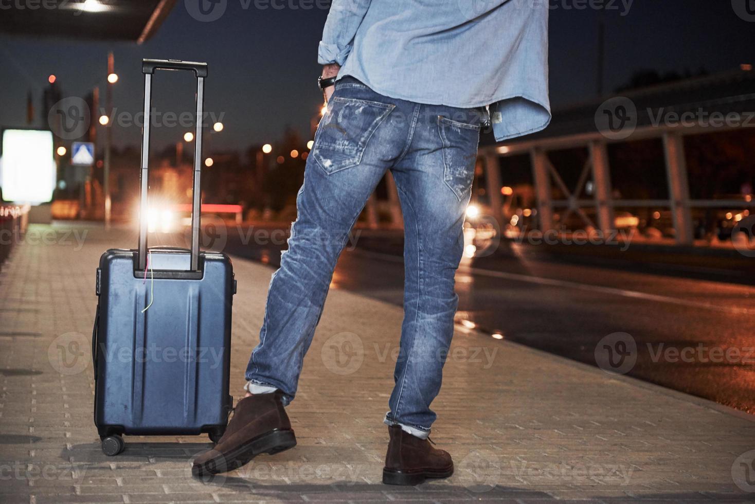 Viajero masculino con una bolsa de equipaje de pie en la noche y pidiendo el coche. foto