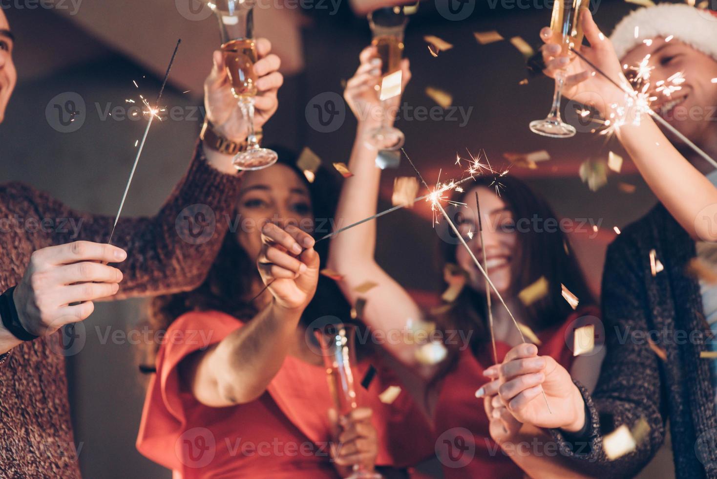 pide un deseo. amigos multirraciales celebran el año nuevo y sostienen luces de bengala y vasos con bebida foto