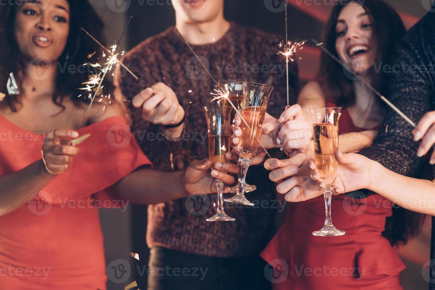 Rejoice as in childhood. Multiracial friends celebrate new year and holding bengal lights and glasses with drink photo