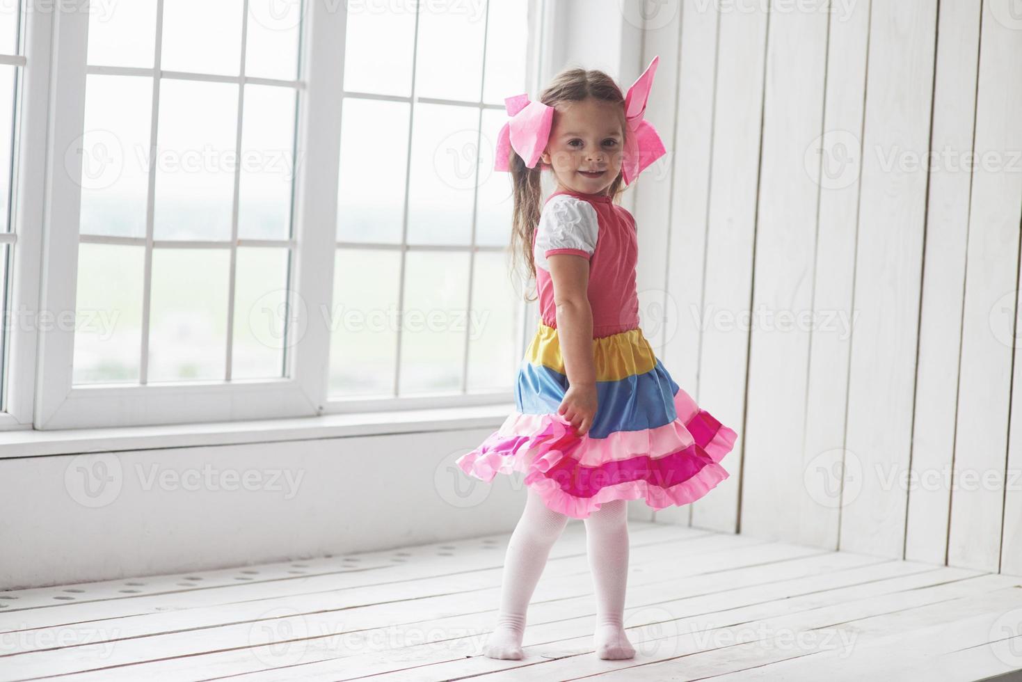 Child standing beside the windows in white room and posing for the photo