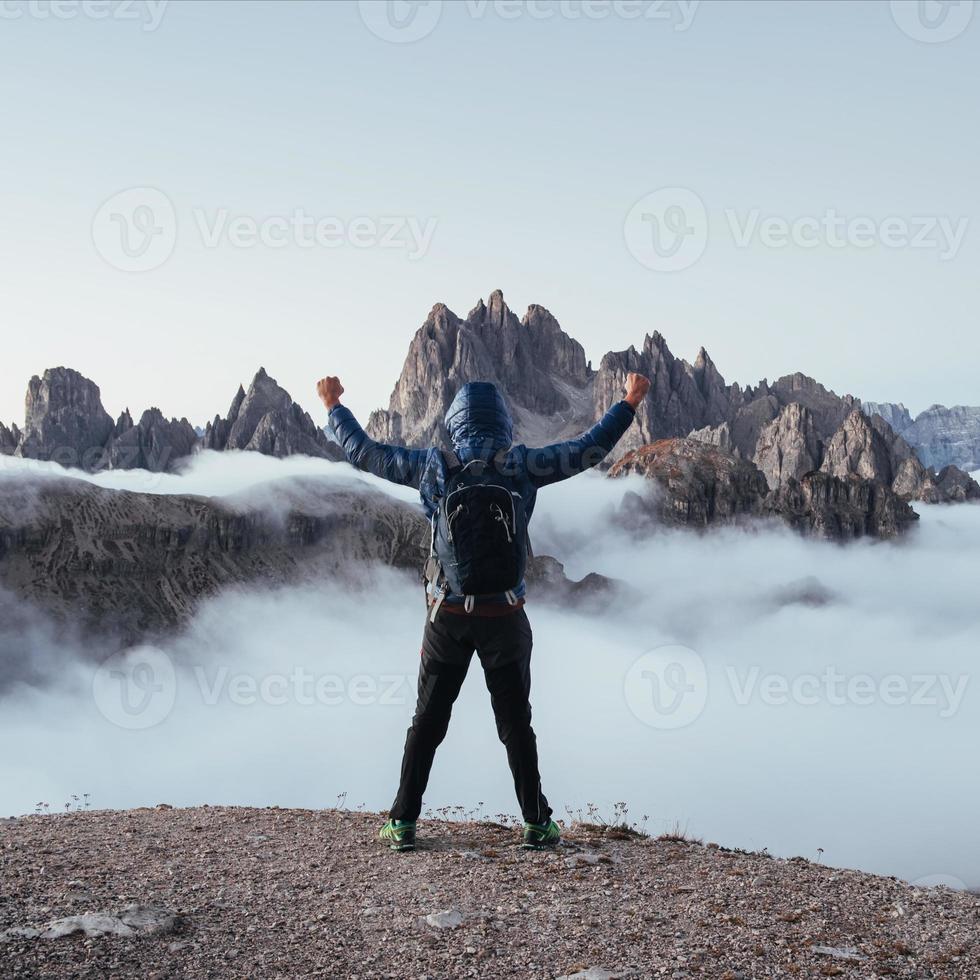 Touristic man raised his hands up on the beautiful daylight mountains full of fog photo