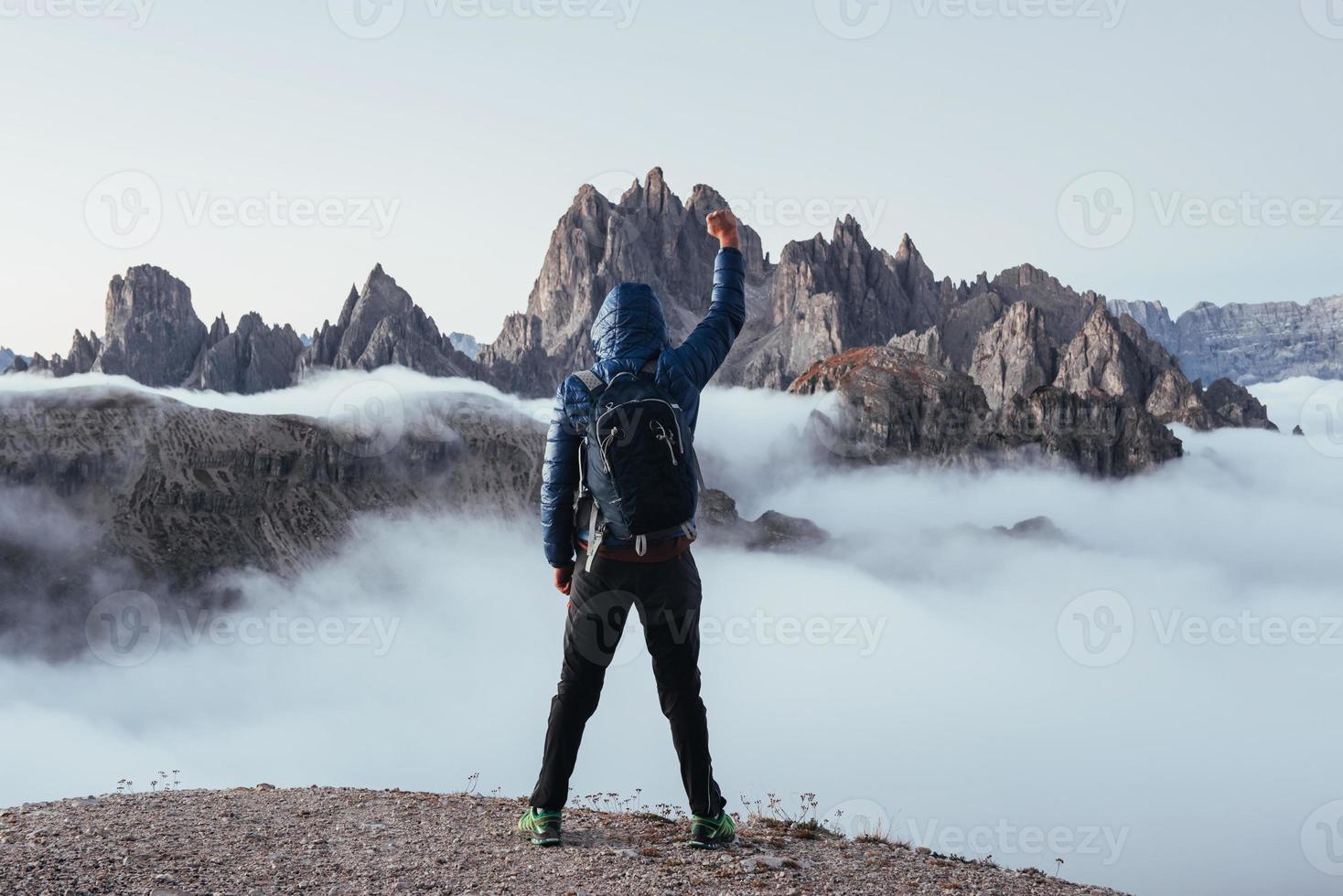 Conquest that hill. Touristic man raised his right hand up on the beautiful daylight mountains full of fog photo