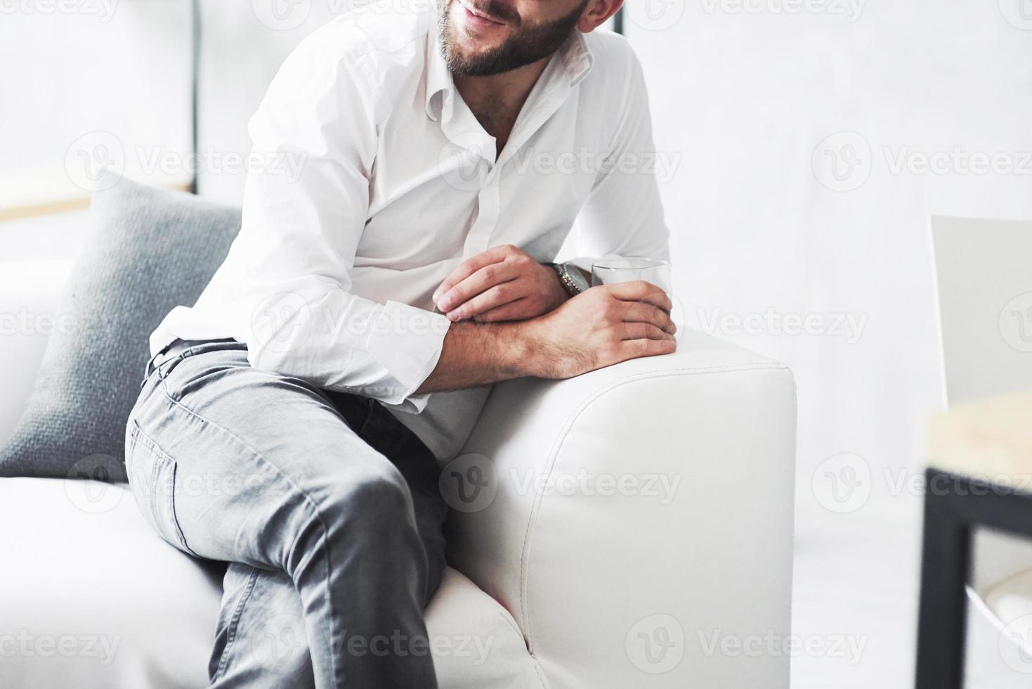 Cropped photo of young businessman in classic wear sitting on the sofa with whiskey glass in the hand
