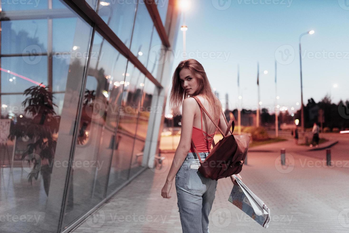 vamos a venir conmigo, conozco el camino corto. Joven viajera sosteniendo el mapa y caminando hacia el lugar al atardecer. foto