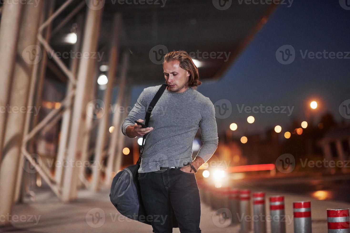 Calling number. Man with long hair and travel baggage waiting for the taxi to pick him up photo