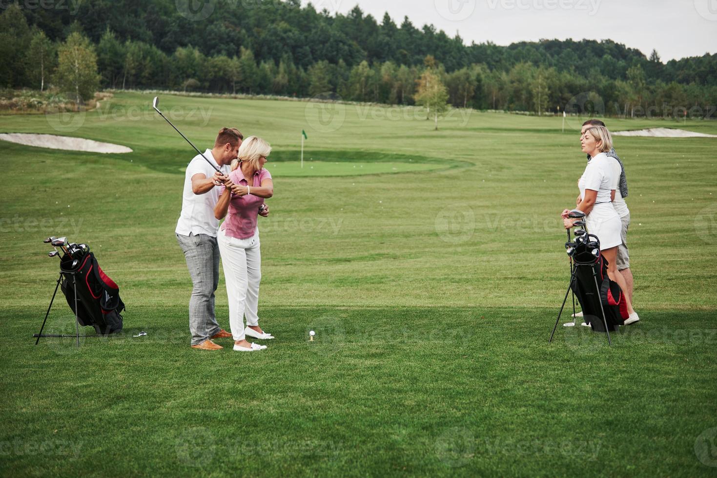 niña jugando al golf y golpeando con el putter en verde. su maestra le ayuda a explorar la técnica y a hacer sus primeros golpes foto