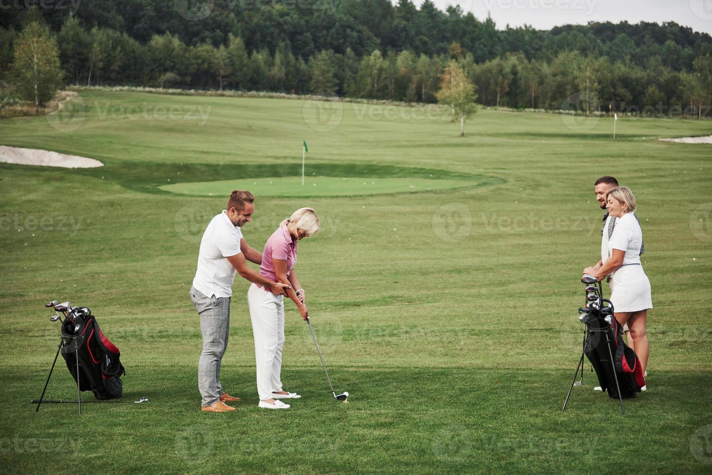 Girl playing golf and hitting by putter on green. Her teacher helps to explore the technique and make her first strikes photo