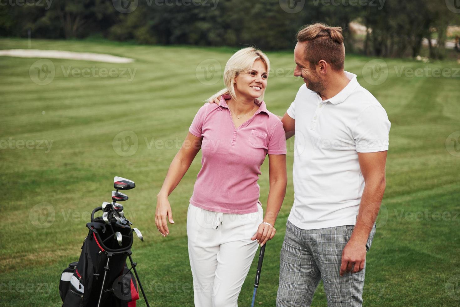 Sportive couple playing golf on a golf course, they stand to the next hole photo