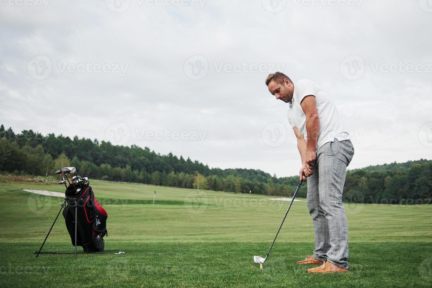 Pro golf player aiming shot with club on course. Male golfer on putting green about to take the hit photo