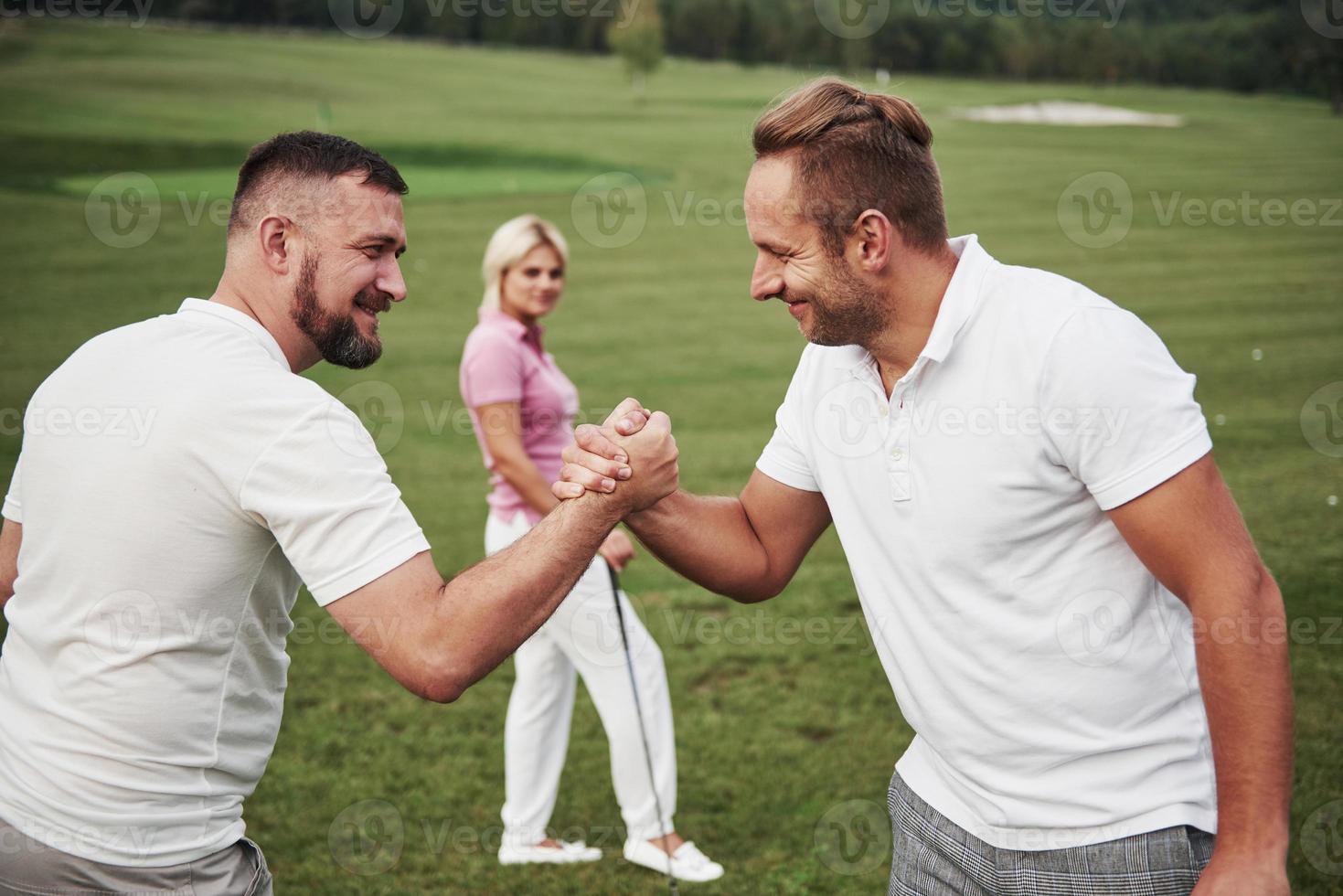 Three players play on the golf course. The team congratulates and shakes hands with each other photo