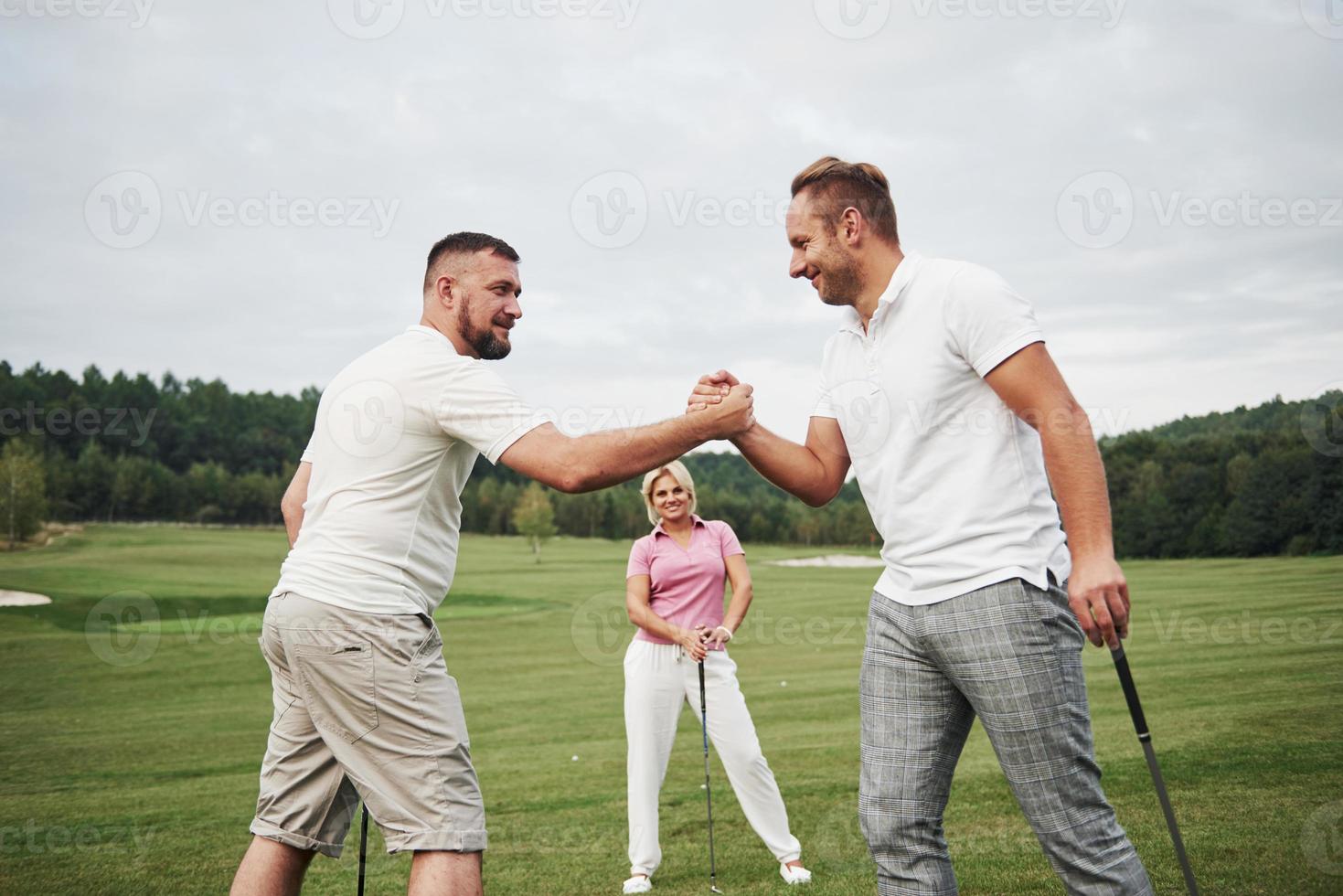 Three players play on the golf course. The team congratulates and shakes hands with each other photo