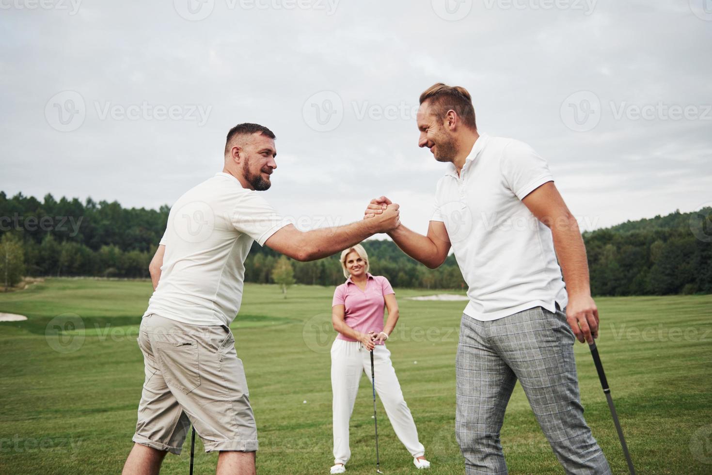 tres jugadores juegan en el campo de golf. el equipo se felicita y se da la mano foto