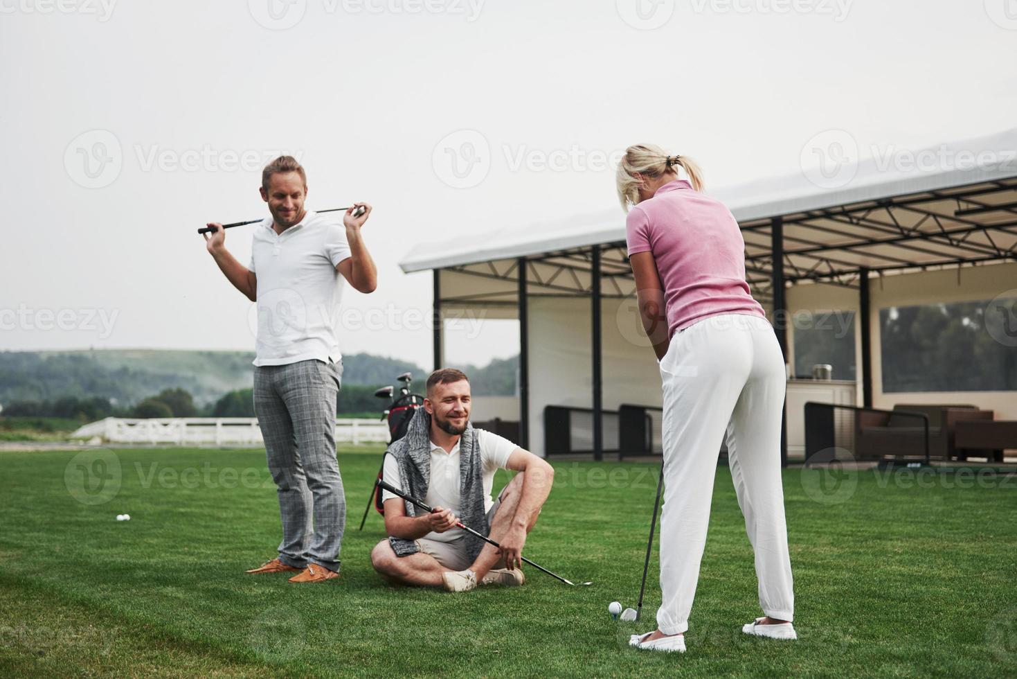 Girl playing golf and hitting by putter on green. Her teacher helps to explore the technique and make her first strikes photo