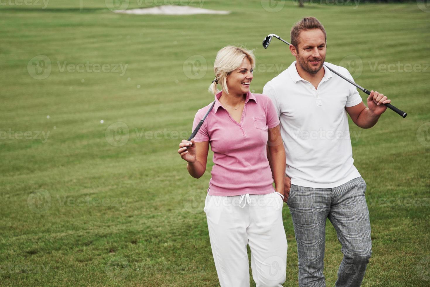 Sportive couple playing golf on a golf course, they stand to the next hole photo