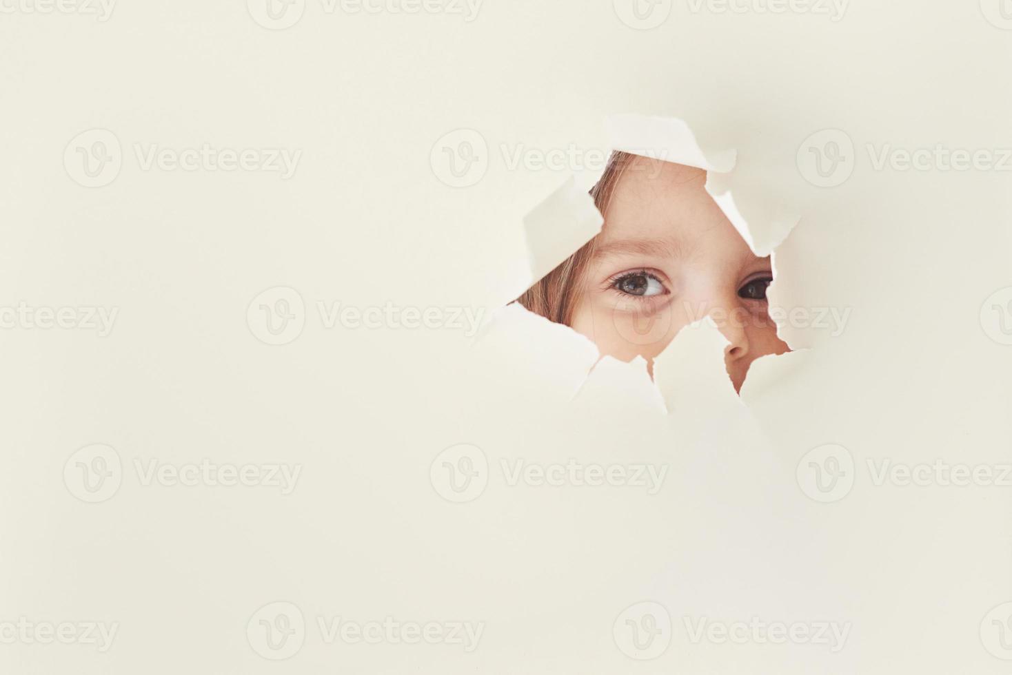 curiosidad infantil. Agujero rasgado en papel blanco con ojos de niña mirando a través foto