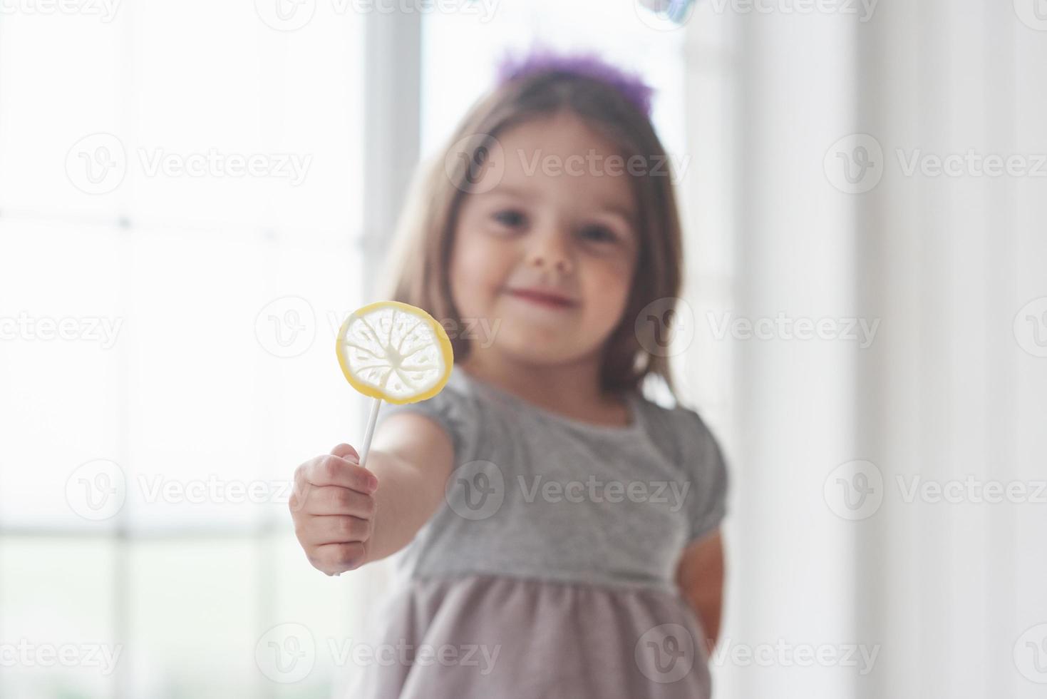 Niña sosteniendo un caramelo amarillo en su mano derecha sobre fondo blanco. foto