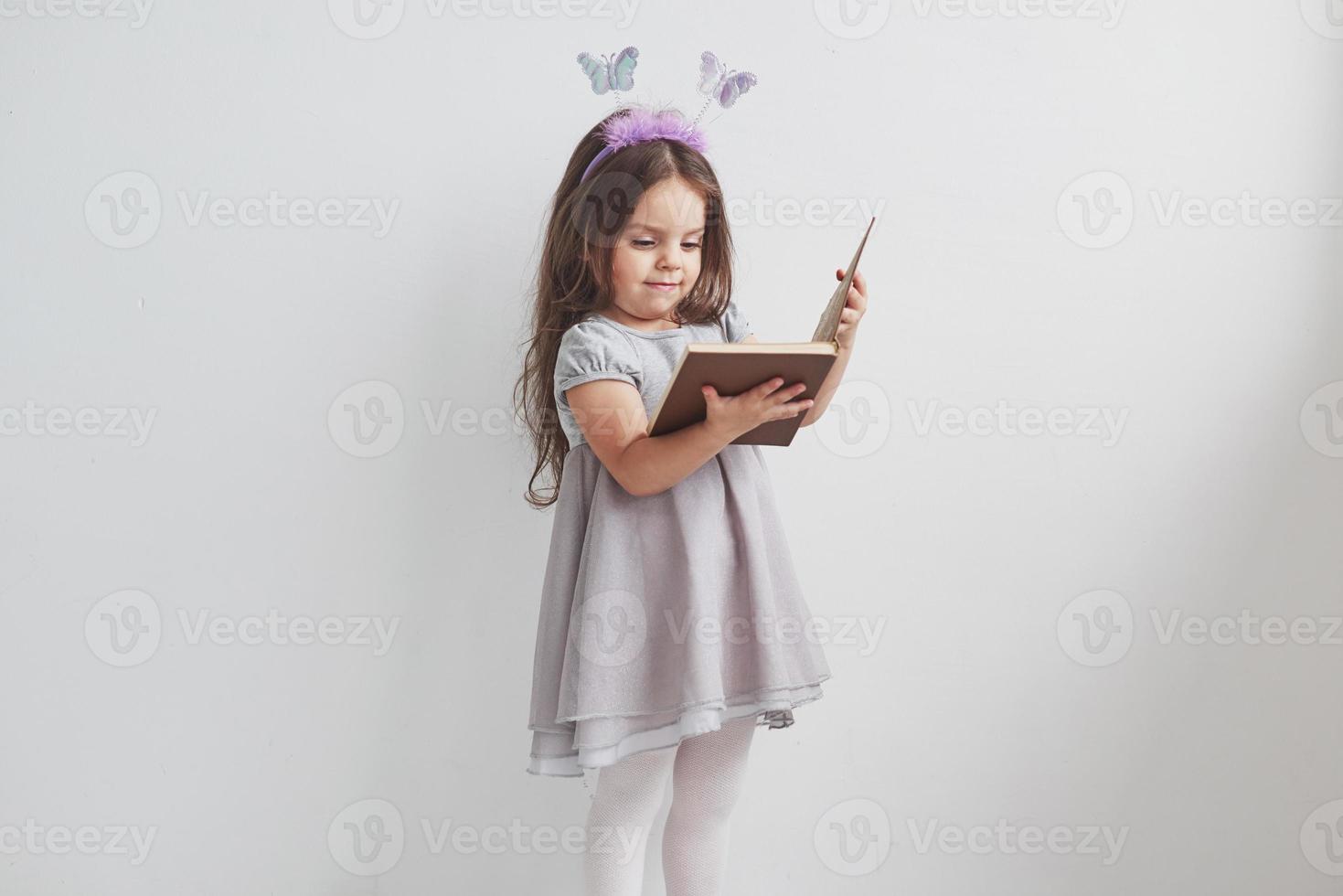 Niña mira ilustraciones en el libro escolar en la habitación con fondo blanco. foto