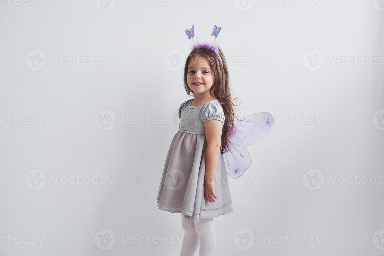 Encantadora niña en el traje de hadas de pie en la habitación con fondo blanco. foto