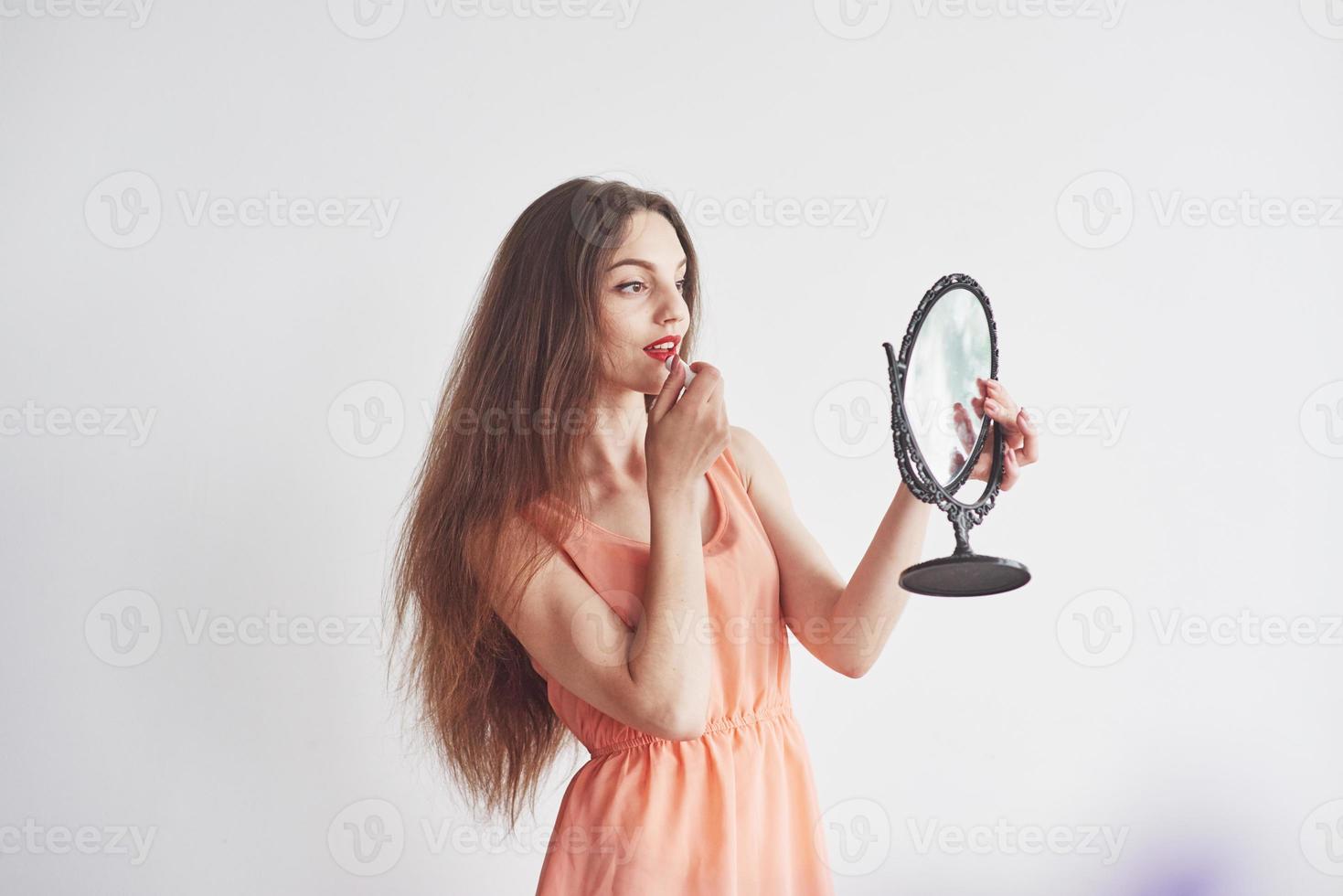 Hermosa joven sosteniendo un espejo y haciendo maquillaje foto