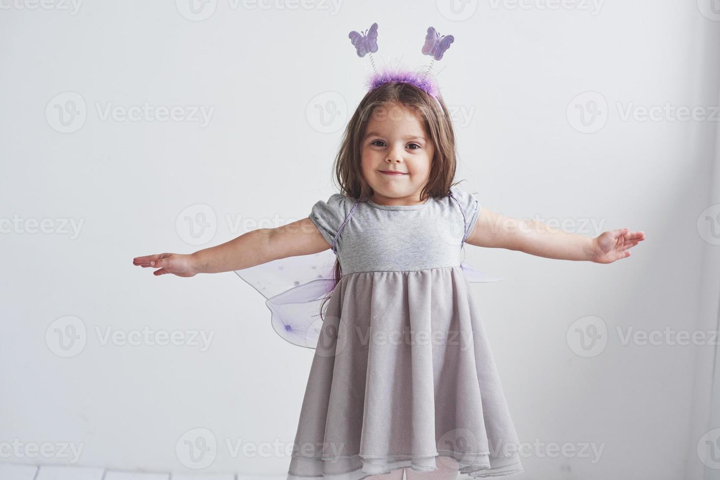 creo que puedo volar. Encantadora niña en el traje de hadas de pie en la habitación con fondo blanco. foto