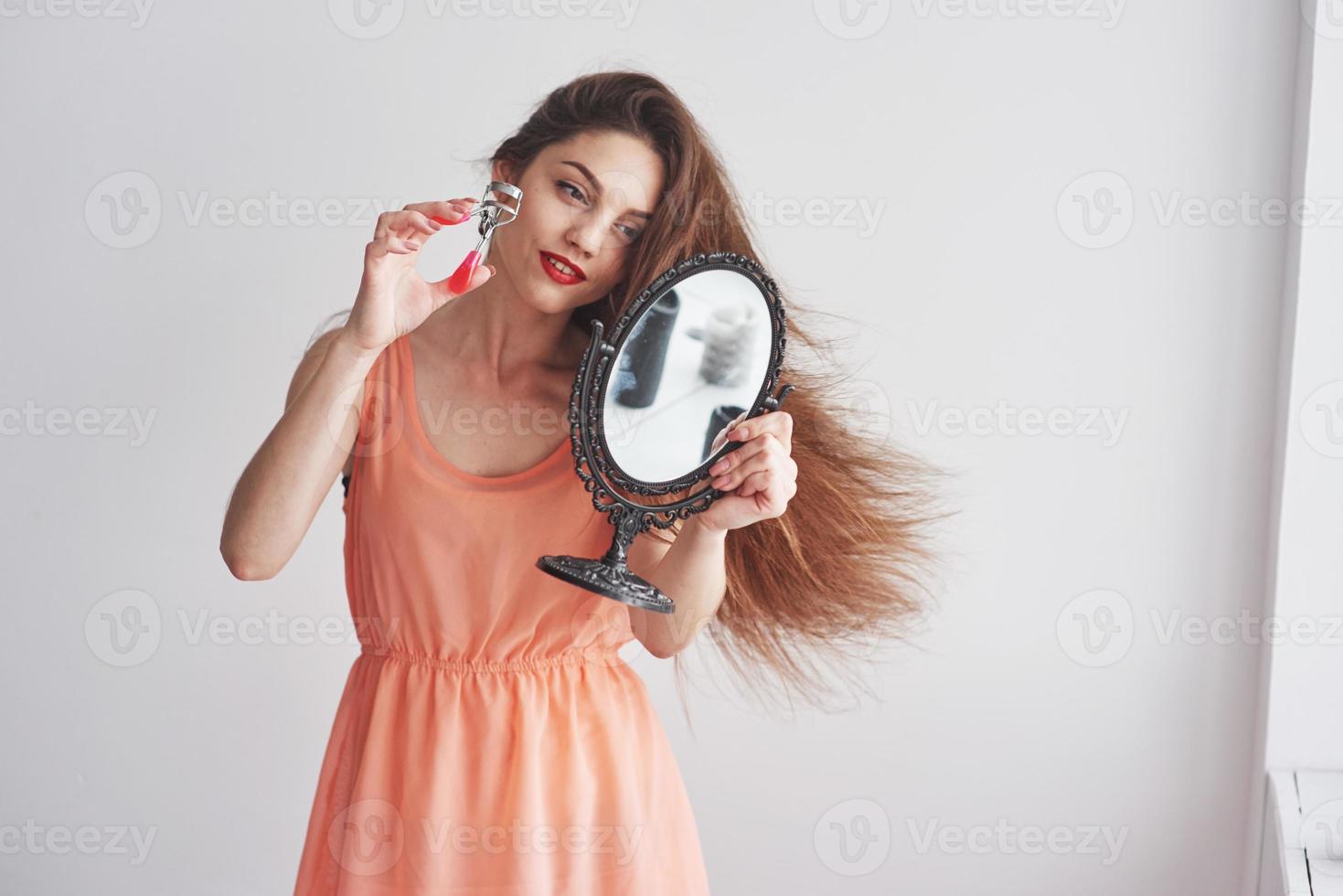 Front view. Young beautiful woman holding a mirror and looking at the brows tool photo