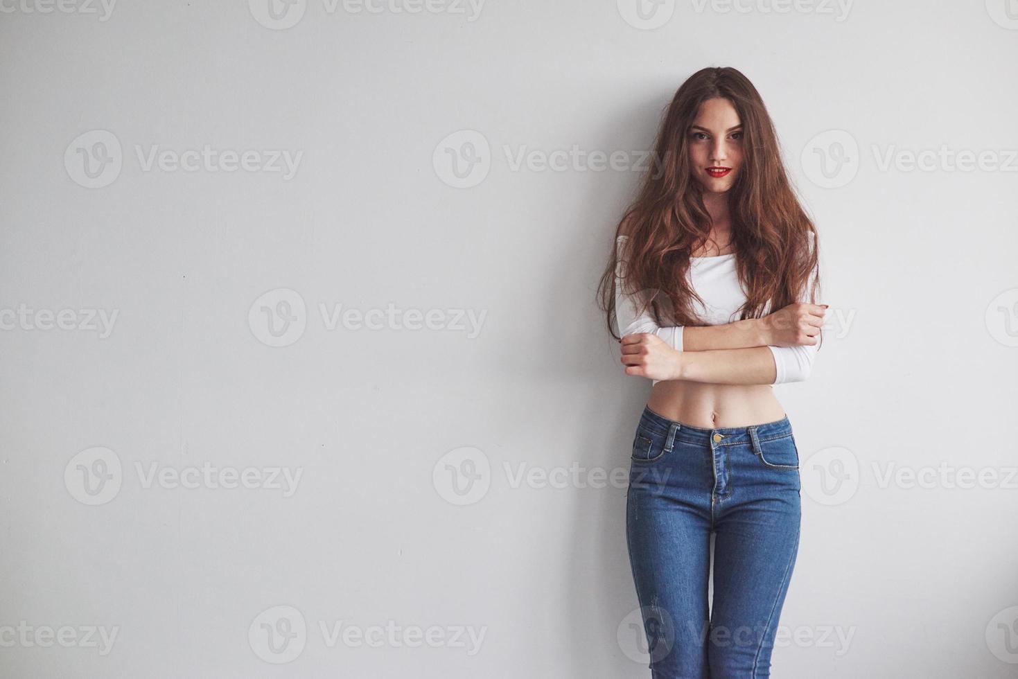 Hot look. Gorgeous smiling young woman standing with hands crossed leaning against the wall photo