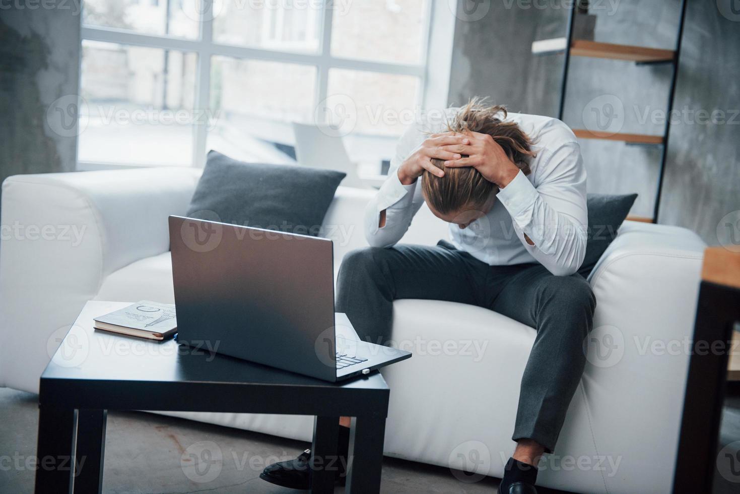 Hombre estresado sentado en el sofá frente a la computadora portátil ha bajado la cabeza foto