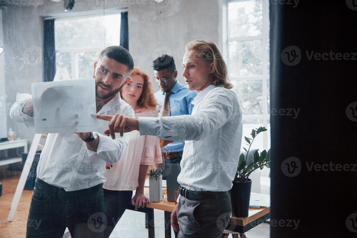 Photo through the glass. Young multiracial team in official wear at office looking at price list