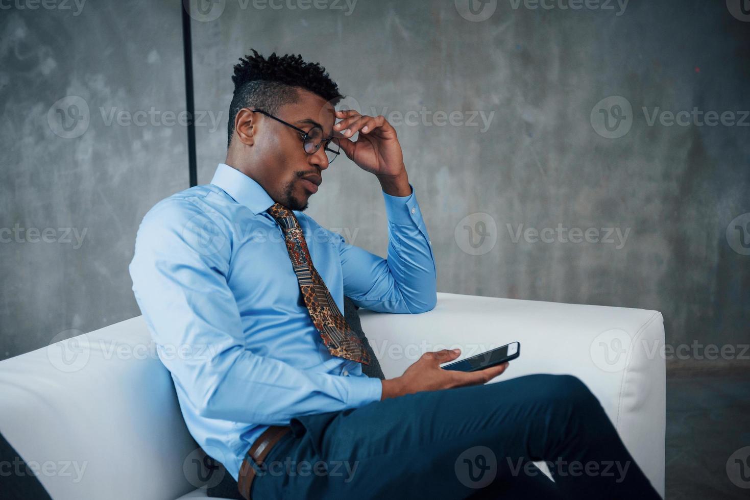 tiempo de relajación. Close Up retrato de joven afroamericano con gafas y ropa clásica sentado en el sofá foto