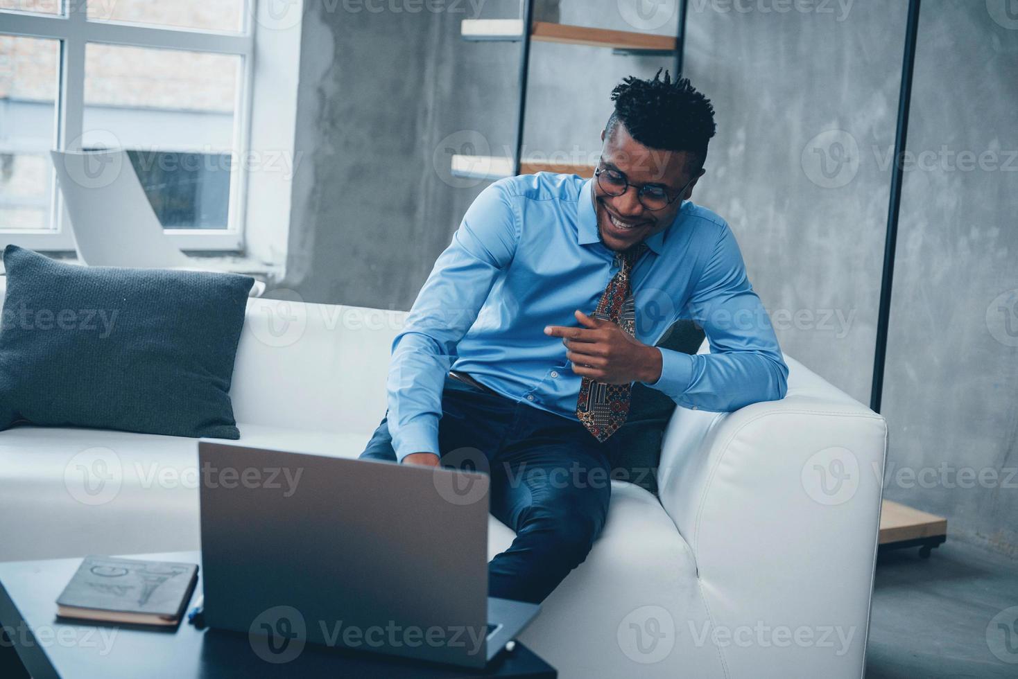 Feeling good. Photo of young afro american guy in glasses and classic wear sitting in a front of laptop