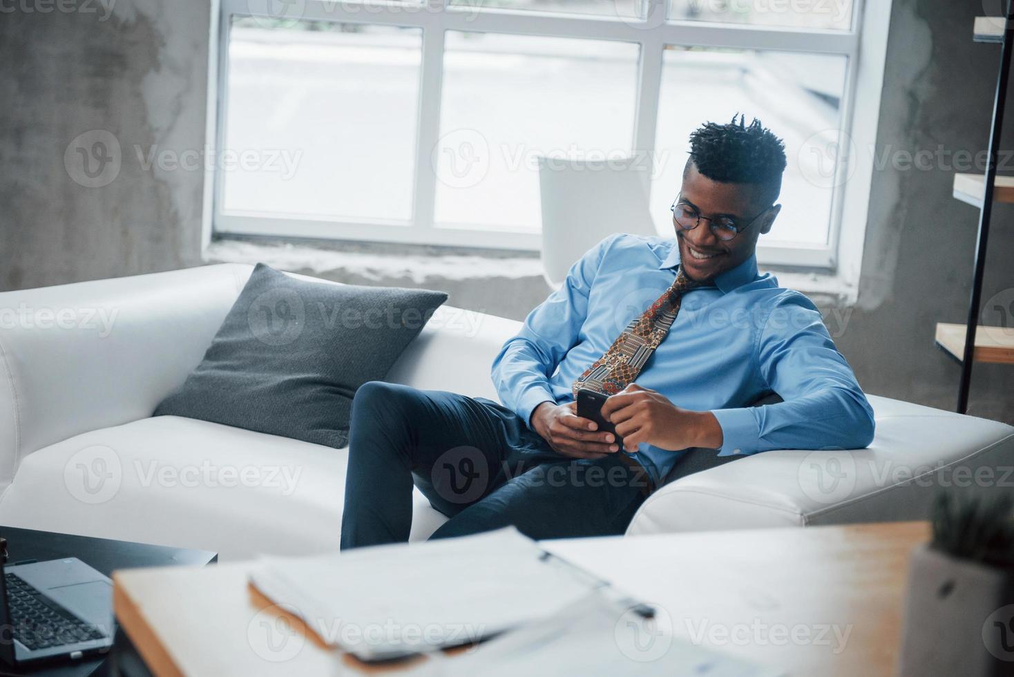 Close up. Smiling afroamerican guy sitting on the couch and looking at his smartphone photo