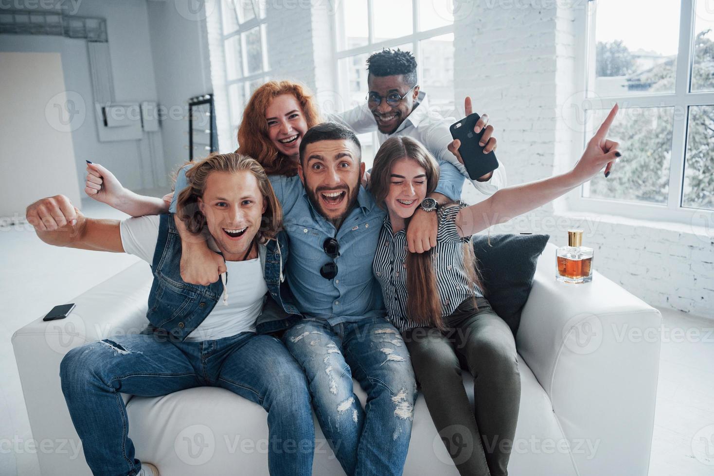 Hands up. Funny young friends having fun sitting on the sofa in the white interior photo