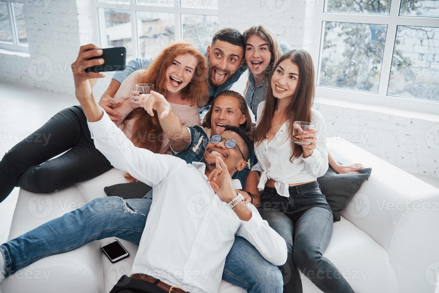 Showing tongues. Cheerful young friends having fun and drinking in the white interior photo